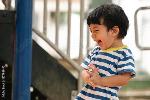 Wallpaper Mural Joyful little Asian boy laughing loudly while playing at the outdoor playground. Happy Asian toddler clapping his hands at a public park playground. Pure childhood joy. Torontodigital.ca