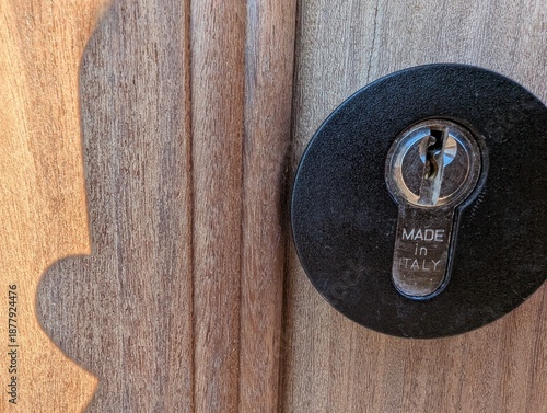 Close-up of a modern door lock on textured wooden door with visible wear from impact, circular black escutcheon and Made in Italy label, ideal for home security, hardware, and design themes.