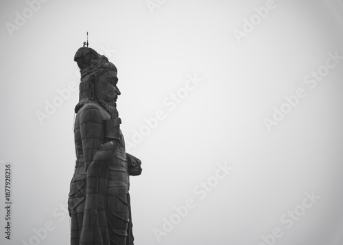 A tall Thiruvalluvar statue standing with wide space for copy text.