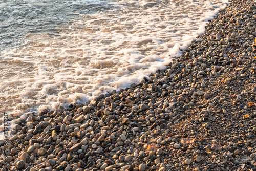Gentle waves wash over smooth pebbles along the shoreline of Gimli, Manitoba, Canada on Lake Winnipeg, glowing in warm natural light on a sunny fall day