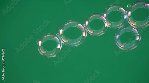 Transparent soap bubbles floating diagonally across green screen