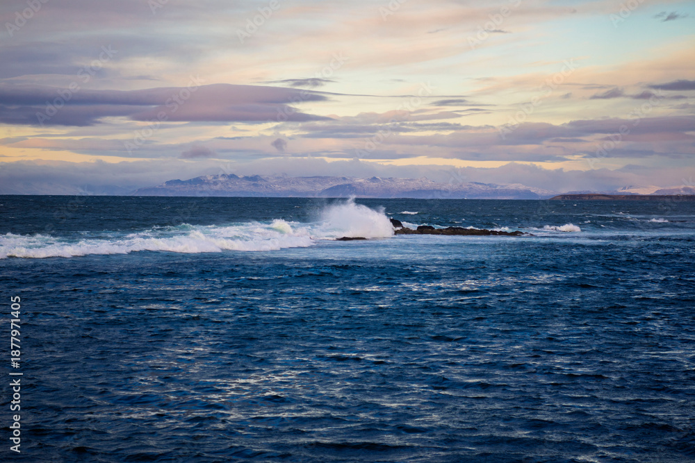 Obraz premium Waves Breaking on Rocky Reef with Distant Mountains and Dramatic Sky, Iceland