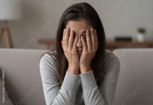 A young woman sitting on a couch with her hands covering her face