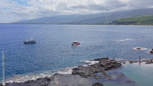 Aerial drone footage using a dolly zoom effect while moving forward and zooming out, focusing on a diving boat near natural pools along the coastline in Cap La Houssaye Reunion Island.