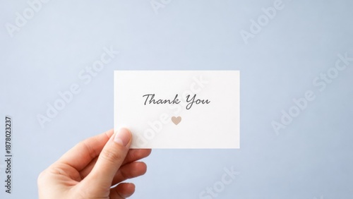 Wallpaper Mural A hand holding a simple "Thank You" card with a heart, set against a soft blue background. Torontodigital.ca