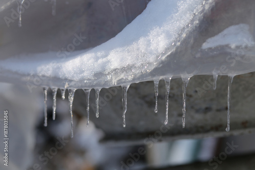 Frozen construction plastic sheeting under a layer of snow and hanging icicles melting in the sunlight.