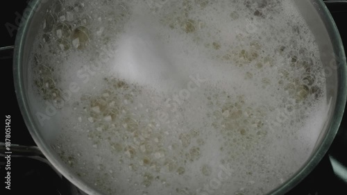 Water roils in a pot, creating foam and bubbles. Pasta is introduced and cooks in the simmering liquid on a stovetop