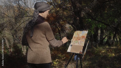 The artist paints an autumn forest with watercolor in the open air on a warm sunny day