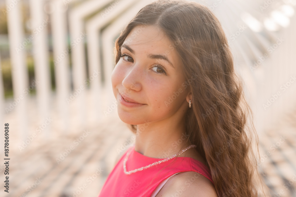Obraz premium beautiful teenage brunette girl with long hair, smiling, looking at the camera during a summer walk