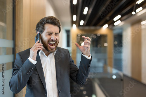 Slika na platnu Businessman gesturing with a clenched hand, intensely shouting into his mobile p