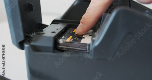 Micro cassette insert into an old telephone answering machine, fax, analog recording of a conversation, retro device, side-view close-up