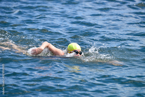 woman swimming in open water with orange safety buoy, female athlete practicing front crawl in the ocean, outdoor swimming training with tow float for safety, swimmer with pink cap in turquoise water 