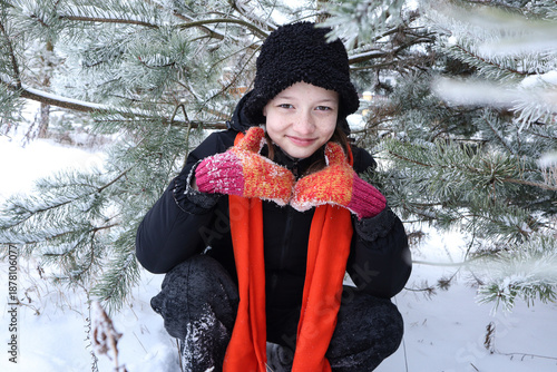 A thirteen-year-old girl in a black, bright orange scarf, and mittens among snow-covered trees during a winter walk