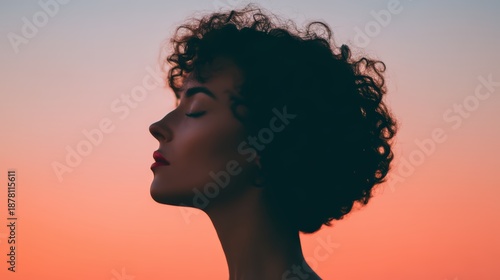A silhouetted profile of a woman against a vibrant sunset, showcasing her curly hair and serene expression.