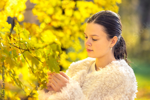 Beautiful young woman with autumn yellow leaves. Portrait of joyful woman playing with tree leaves in park during autumn. Happy girl wearing red turtleneck and headband and playing with leaves outside