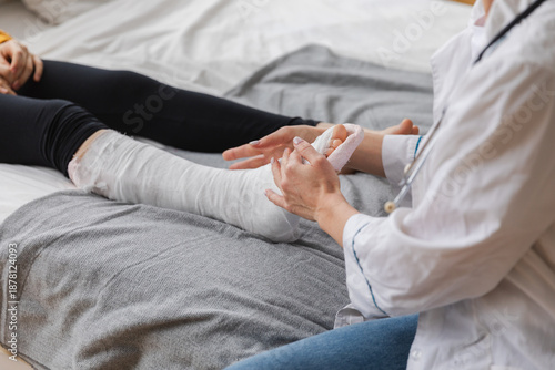 Girl with broken leg and doctor in clinic. Traumatologist orthopedist examines child leg in medical office. Doctor examining girl with medical plaster leg cast after broken ankle injury Rehabilitation