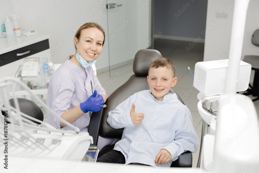Obraz premium Happy dentist and child patient showing thumbs up in dental clinic