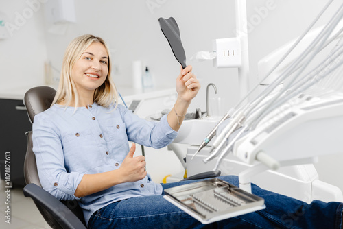 Patient admiring smile after dental checkup using small mirror in modern clinic