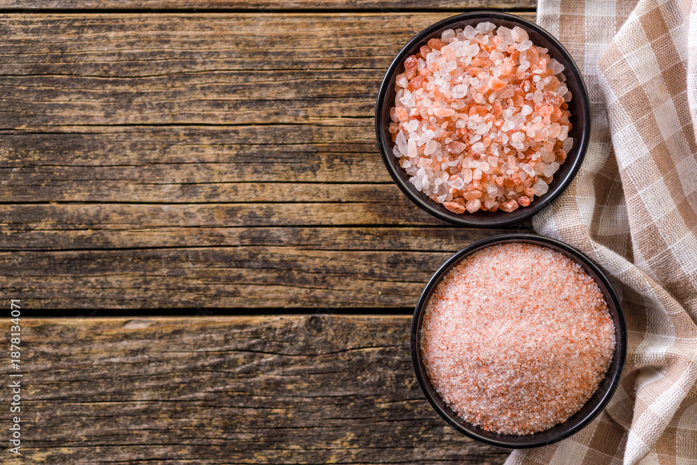 Naklejka premium Pink Himalayan salt in bowl on wooden table. Top view.