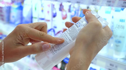 Close up of female hands holding a cosmetic tube and carefully reading the ingredients list on the label while standing in a store, making an informed choice for her beauty and skincare routine