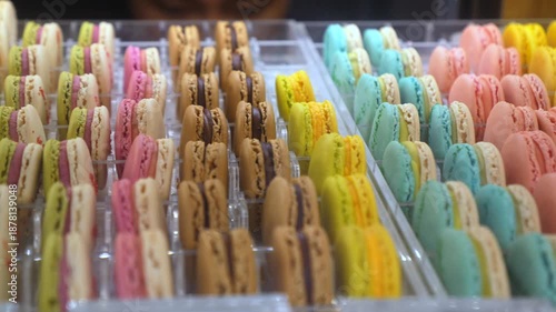 Rows of delicious and colorful french macarons with various flavors standing vertically in a transparent display case inside a bakery, showcasing the delightful and sweet confectionery