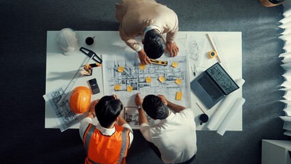 Top down aerial view of smart architect engineer team pointing and discussing about building construction. Group of diverse people working together to plan and design by using blueprint. Alimentation.