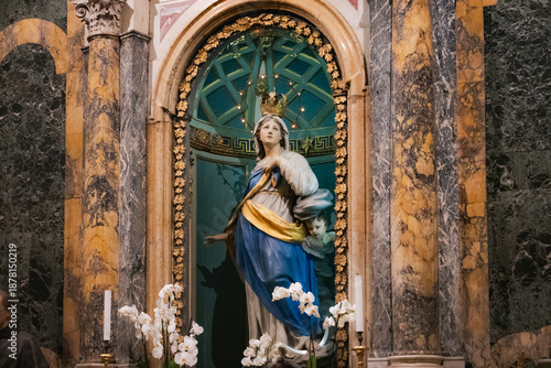 Historic Baroque statue of the Immaculate Conception inside the Basilica di San Francesco in Ravenna, Italy. The marble monument features a blue and gold niche background.