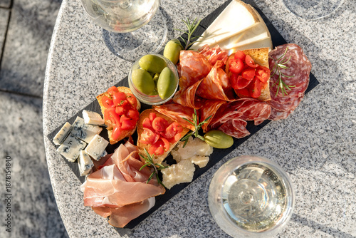 Outdoor Patio Gourmet charcuterie board with meats prosciutto ham, salami, green olives and cheese with white wine or prosecco aperitif or dinning outdoor Italian style