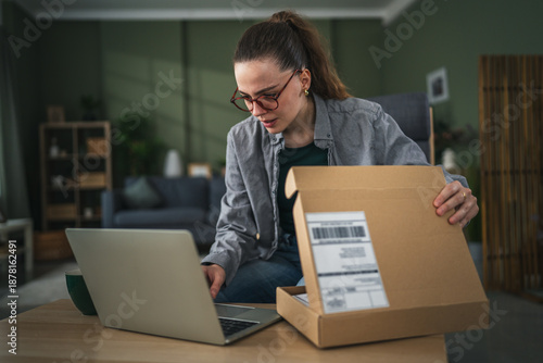 Quadro su tela Woman unpacking delivery with laptop showing disappointment