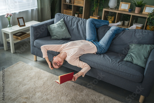 Woman lying upside down on sofa reading book at home