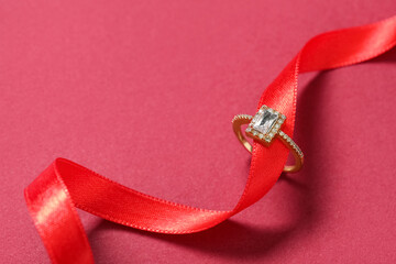 Engagement ring with ribbon on red background, closeup. Valentine's day celebration