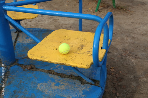 Yellow tennis ball placed on blue and yellow playground equipment at a park in daytime