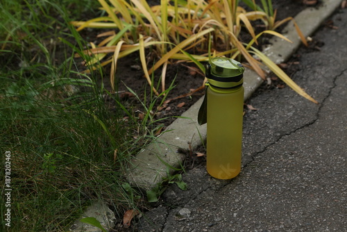 Water bottle placed next to plants on a pathway during daytime in a residential area