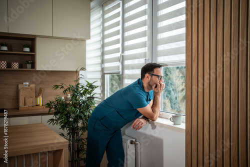 Valokuva Physician contemplating while looking out window in kitchen