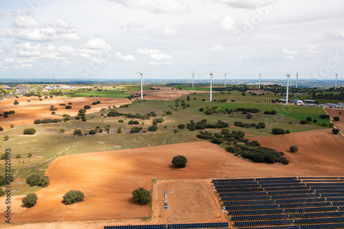 Aerial drone view of sustainable energy landscape with wind turbines and solar panels across farmland producing clean renewable electricity under cloudy sky
