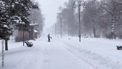 Snow Removal Operation in a Public Park During an Intense Winter Blizzard, Janitors Using Red Shovels to Clear Frozen Walkways for Pedestrians.Extreme Weather Cleaning Service