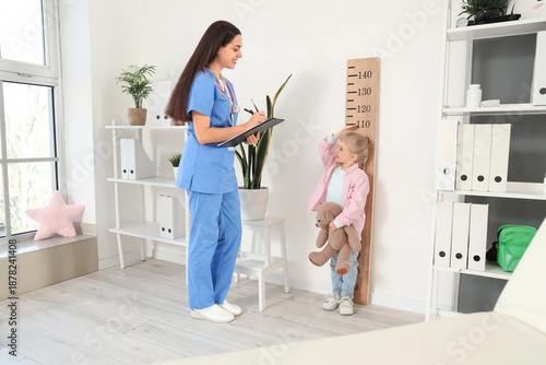 Female pediatrician measuring height of little girl in clinic