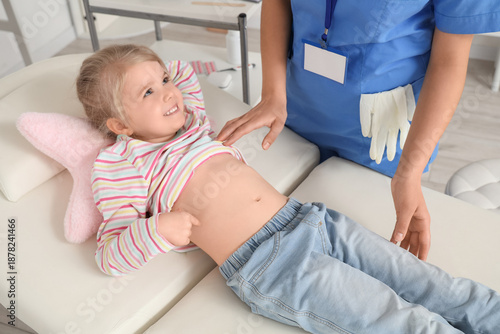 Female pediatrician examining little girl's belly on couch in clinic, closeup