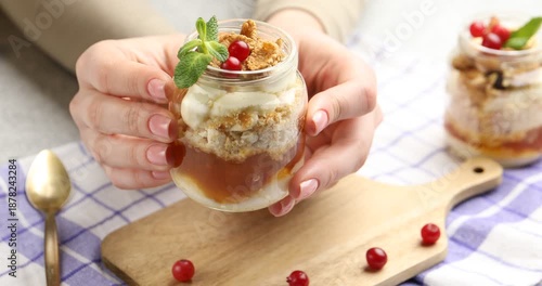 Woman with tasty trifle dessert in glass jar at table, closeup