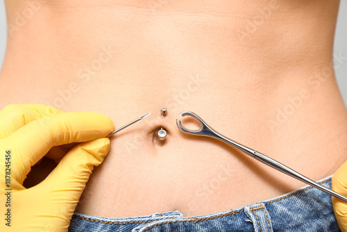 Tableau sur toile Professional doing piercing of young woman's navel on grey background, closeup