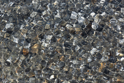 Transparent water flowing over rocks in a mountain stream in Patagonia with sun glare. Concept of fresh drinking water, ecology, abstract texture background