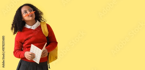 Funny thoughtful African-American schoolgirl with notebook on yellow backgrou...