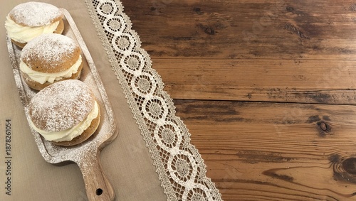 Three Swedish semla buns with powdered sugar on rustic board – traditional pastry for Fettisdagen (Fat Tuesday) with copy space