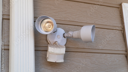 фотографія White twin floodlight motion sensor outdoor lighting fixture mounted on the siding of a residential home exterior