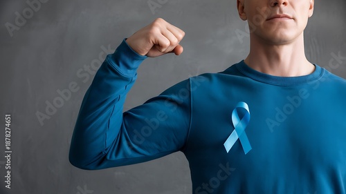 Young man in blue shirt flexing bicep with a blue awareness ribbon pinned to his chest