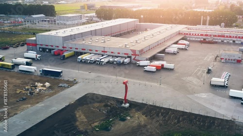 Drone Shot: Logistics Sorting Terminal with Multiple Trucks at Warehouse Loading Bays | Distribution Center Complex During Golden Hour Sunset | Supply Chain Hub with Parked Cargo Vehicles