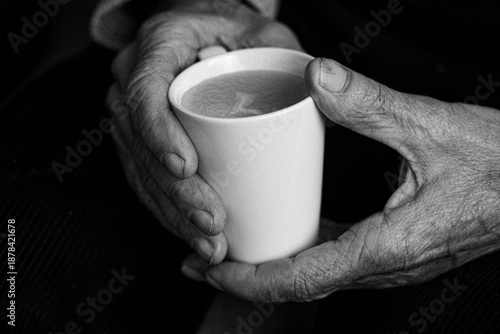 Elderly hands holding warm cup of coffee in black and white