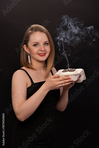A woman in a black dress blows out a candle on a bento cake. Smoke on a black background. A girl's birthday, happiness, a gift. High quality photo