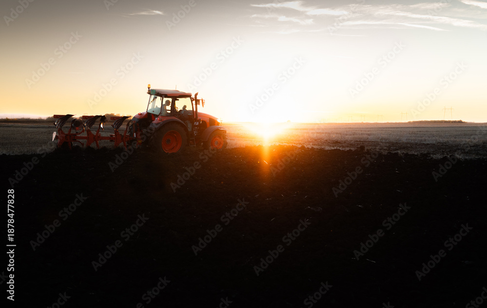 Fototapeta premium Tractor plowing field the land at sunset