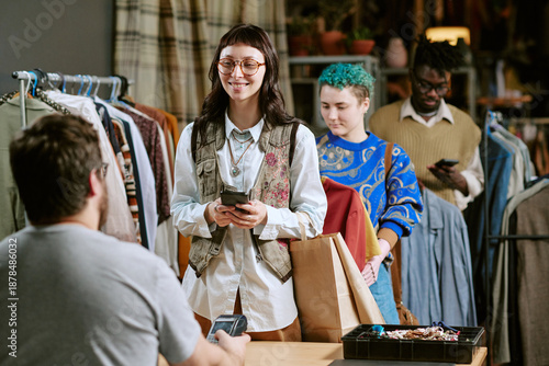 Konstfotografi Young biracial woman smiling while holding smartphone and shopping bag, standing